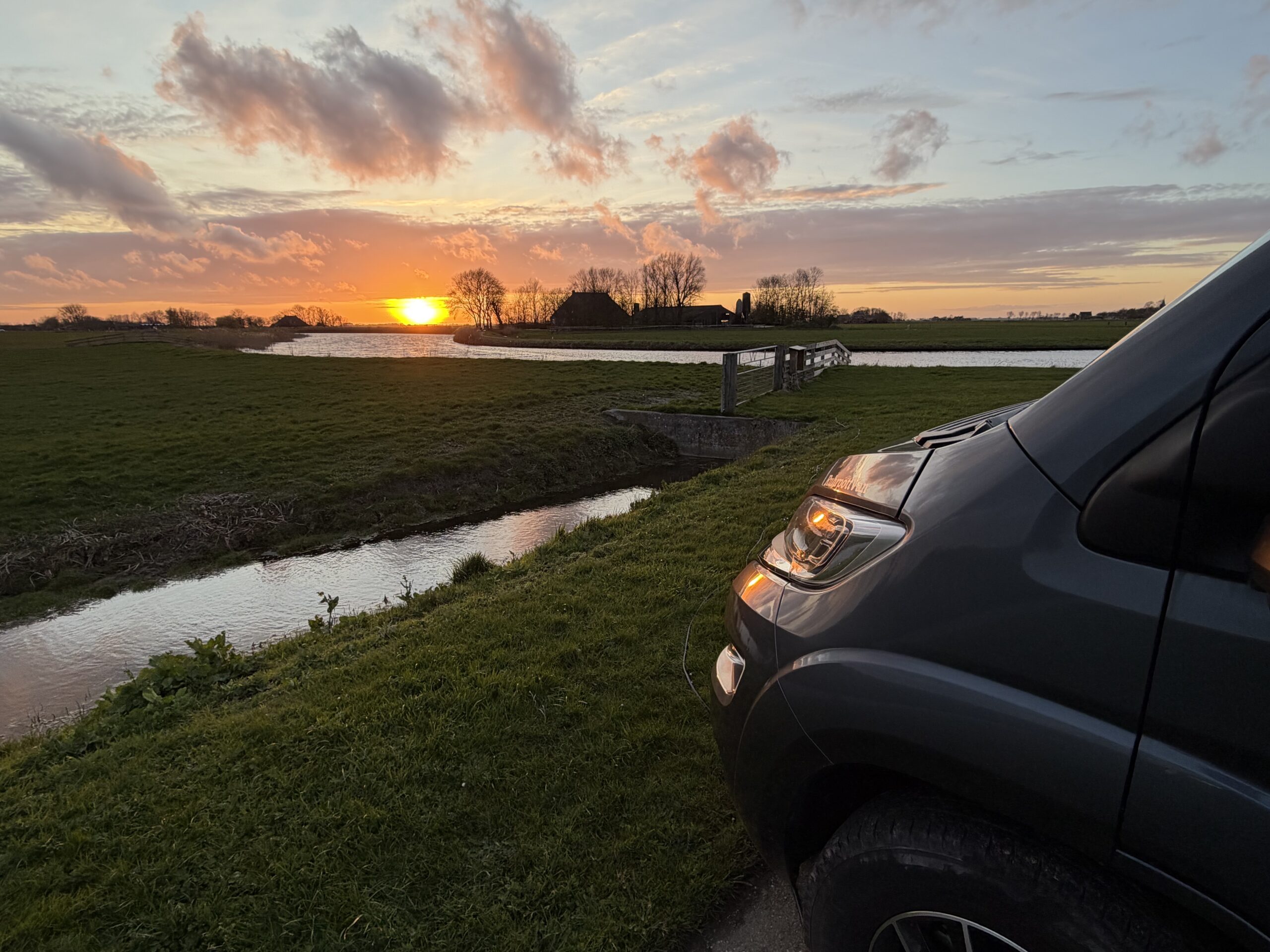 Grauer Campervan steht vor einem Sonnenuntergang